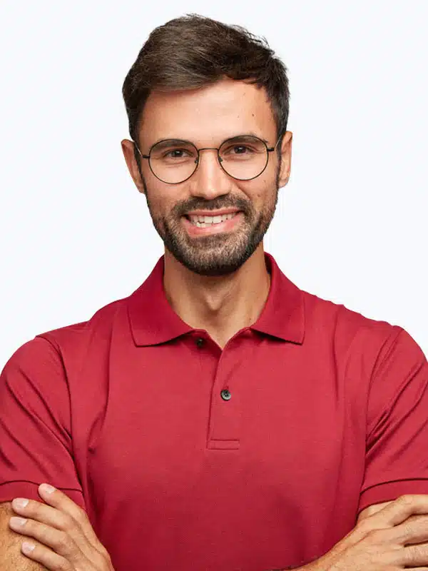 Man with short brown hair, beard, and glasses, wearing a red polo shirt, smiles while crossing his arms.