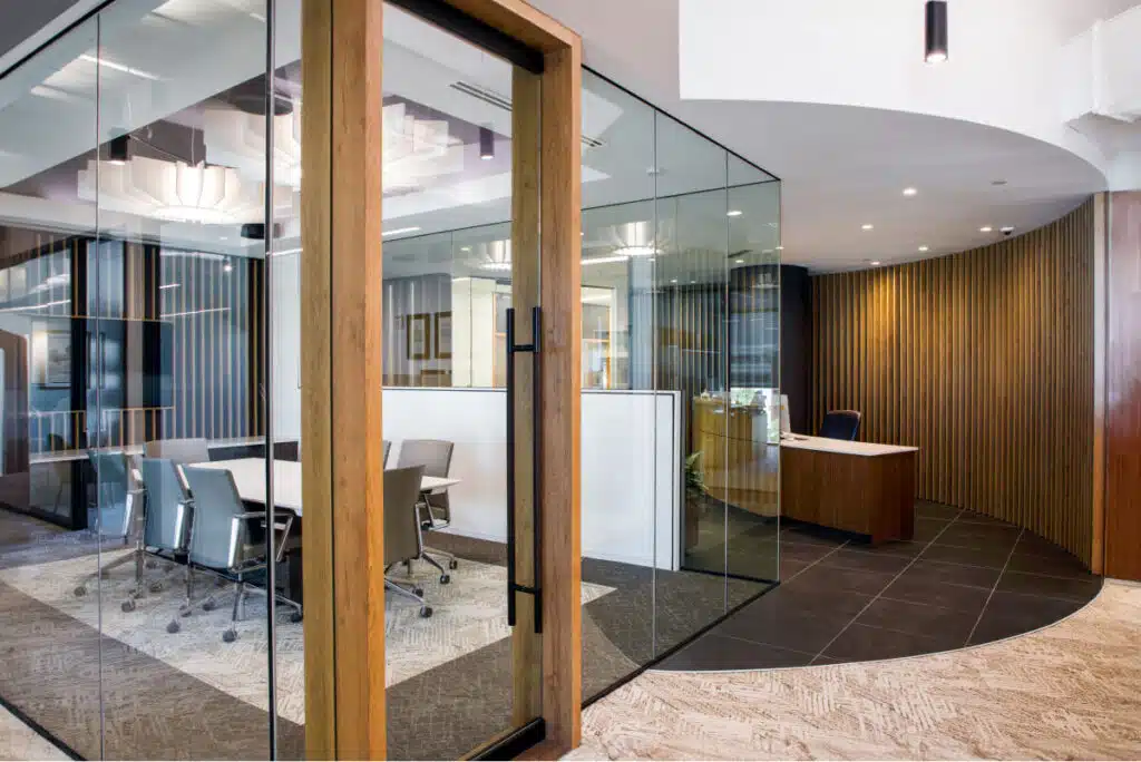 Modern office space featuring a conference room with glass walls and wooden accents, adjacent to a reception desk area with curved wooden paneling.